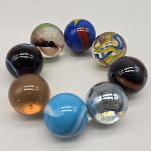 May include: A collection of nine colorful marbles. The marbles feature a variety of colors, including blue, yellow, red, black, brown, and clear. Some marbles have swirling patterns, while others are solid in color. The marbles are arranged in a circular pattern.