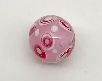 May include: A round, pink glass bead with a glossy finish. The bead features a pattern of white and deep pink circles and dots. This decorative bead is suitable for jewelry making and other craft projects.