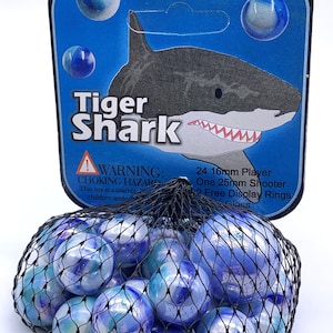 Puede incluir: Una bolsa de 24 canicas de vidrio azul y blanco con una ilustraci&oacute;n de tibur&oacute;n tigre en el empaque. El empaque tambi&eacute;n incluye el texto "Tiger Shark", "WARNING: CHOKING HAZARD", "This toy is a marble", "children under", "24 16mm Player", "One 25mm Shooter", "2 Free Display Rings", y "Glass".