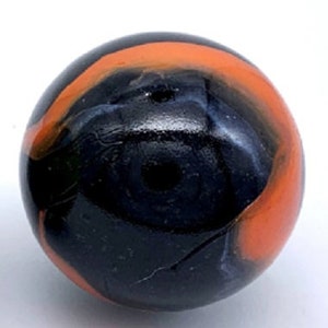 May include: A black and orange glass marble with swirling patterns. The marble has a dark blue and black center with a thin orange band around the edge.