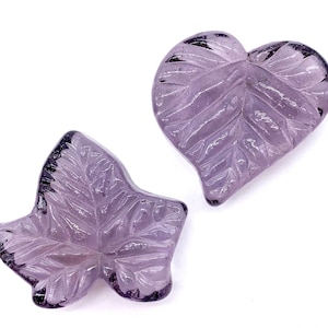 May include: Two purple glass leaf-shaped ornaments. One is a heart shape and the other is a double leaf.