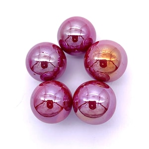 May include: Five iridescent glass marbles in shades of pink and purple. The marbles are arranged in a circle on a white background.