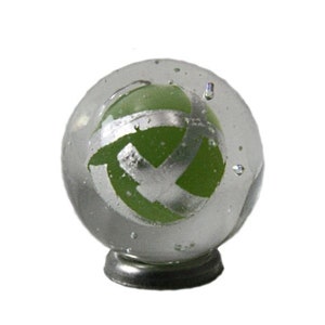 May include: A clear glass marble with a green and silver swirl design. The marble is sitting on a small metal stand.