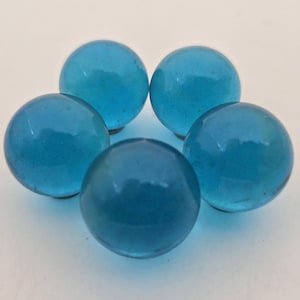 May include: Five translucent, round, light blue glass marbles arranged in a circular pattern. The marbles have a smooth, glossy surface and are slightly different shades of blue. The marbles are a classic toy or decorative item.