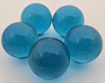 May include: Five translucent, round, light blue glass marbles arranged in a circular pattern. The marbles have a smooth, glossy surface and are slightly different shades of blue. The marbles are a classic toy or decorative item.