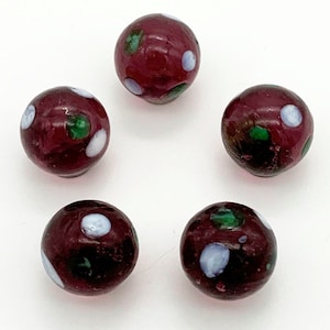 May include: Five round glass beads with a burgundy base and white and green polka dots.