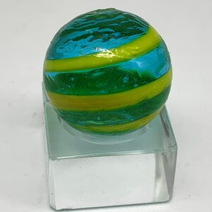 K&ouml;nnte beinhalten: Eine farbenfrohe Glaskugel mit wirbelnden B&auml;ndern in Gr&uuml;n, Gelb und Blau. Die Kugel ist kugelf&ouml;rmig und ruht auf einem transparenten, rechteckigen St&auml;nder. Die lebendigen Farben und das einzigartige Design machen sie zu einem dekorativen Artikel.