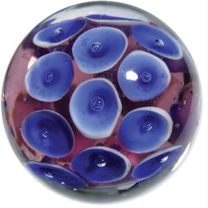 May include: A glass marble with a purple base and blue and white circles.