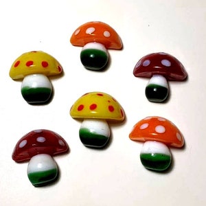 May include: Six glass mushroom figurines with white and red polka dots on the top, white stems, and green bottoms.