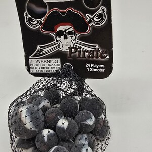 May include: A bag of marbles with a pirate-themed header. The header features a skull and crossbones design with the word "Pirate". The marbles are black and white, and the bag is a black mesh. The header also includes a choking hazard warning.