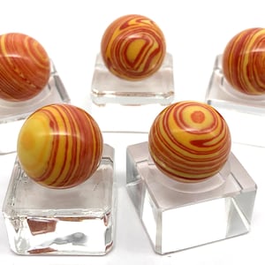 May include: Five red and yellow striped spheres on clear square bases. The spheres are made of polished stone.