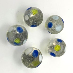 May include: Six glass marbles with a clear, translucent base and colorful spots. The marbles are blue, white, and yellow.