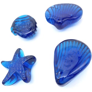 May include: Four blue glass sea-themed ornaments, including a starfish, a clam shell, and two scallop shells.