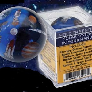 May include: A clear plastic cube with a blue glass sphere inside. The sphere has a detailed image of the solar system, including planets, stars, and spacecraft. The cube has a yellow label that reads "Hold the entire solar system in your hand!" and lists the planets and celestial bodies included in the sphere.