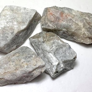May include: Four rough, white, and gray, natural, raw, unpolished, gemstone rocks. The rocks have a variety of shapes and sizes.