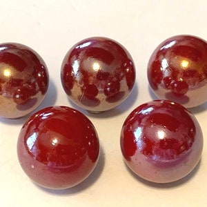 May include: Five glossy, round marbles in shades of burgundy and bronze. The marbles have a reflective surface, with highlights and shadows. The marbles are a classic toy, often used for games or collecting.
