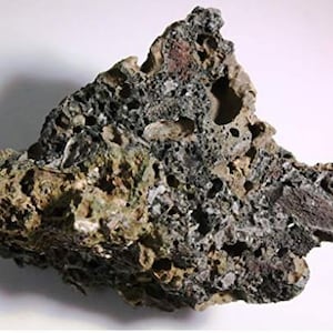 May include: A large, irregularly shaped piece of volcanic rock with a rough, porous surface. The rock is a dark gray color with patches of brown and green.