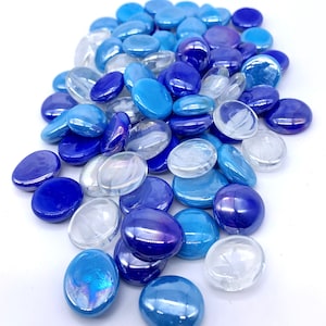 May include: A collection of smooth, oval-shaped glass stones in various shades of blue and clear. The stones range from deep indigo to light turquoise, with some appearing iridescent. These decorative stones are suitable for crafts or home decor.