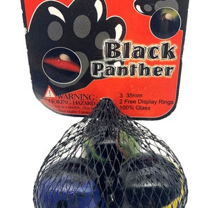 May include: Three black glass marbles with colorful swirls and designs in a black mesh bag. The bag has a red and black label that reads "Black Panther" and includes details like "3 35mm", "2 Free Display Rings", and "100% Glass".