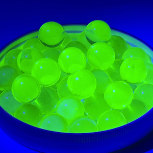May include: A bowl filled with glowing, neon green orbs. The orbs are round and translucent, with a bright, almost luminescent quality. The bowl is a deep blue, creating a striking contrast with the vibrant green spheres. The background is a solid, dark blue.