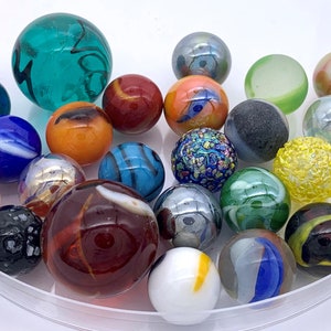 May include: A collection of colorful glass marbles in a clear plastic bowl. The marbles are various sizes and have different patterns and colors, including blue, green, red, yellow, and black.