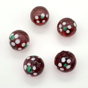 May include: Five glass marbles with a dark purple base and white and green polka dots.