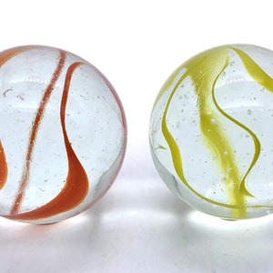 May include: Two glass marbles with swirling patterns. One marble has orange swirls on a clear background, and the other has yellow swirls on a clear background.
