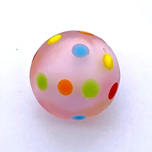 May include: A pink glass ball with colorful polka dots. The dots are yellow, orange, red, green, and blue.