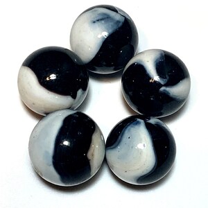 May include: Five black and white swirl glass marbles. The marbles have a white background with black swirls.