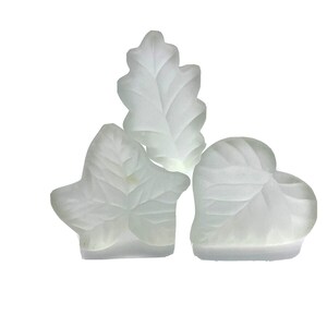 May include: Three white frosted glass leaf-shaped candle holders. The candle holders are in the shape of an oak leaf, a heart-shaped leaf, and a three-leaf clover.