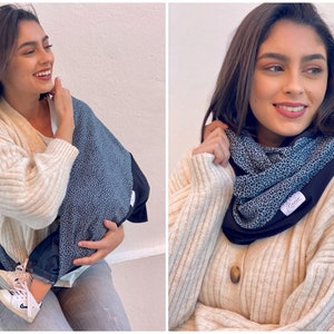 Könnte beinhalten: Eine Frau trägt einen cremefarbenen Cardigan und eine blaue Jeans und hält ein Baby in einem blauen und schwarzen gemusterten Babytrage. Die Trage hat einen schwarzen Gurt und ein weißes Etikett mit dem Wort "Mommy" darauf.