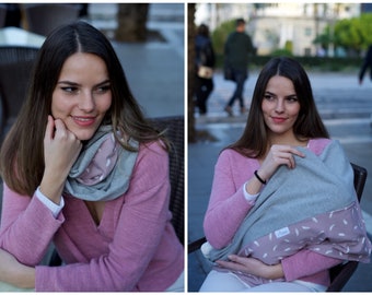 May include: A woman wearing a pink sweater and a gray infinity scarf with a pink feather pattern. She is also holding a matching blanket. The scarf and blanket appear soft and comfortable.