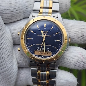 May include: A Pulsar Quartz alarm chronograph watch with a blue analogue dial, gold-tone hands, and a digital display window at the bottom. The watch features a two-tone silver and gold stainless steel link bracelet and a gold-tone bezel.