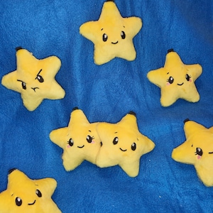 Può includere: Sette giocattoli di peluche a forma di stella gialla con diverse espressioni facciali. Le stelle hanno occhi e bocche neri, e alcune hanno guance rosa.