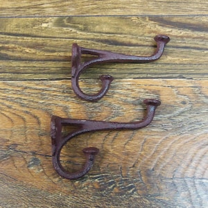 May include: Two rustic brown metal hooks with a decorative scroll design. The hooks are mounted on a wooden surface.