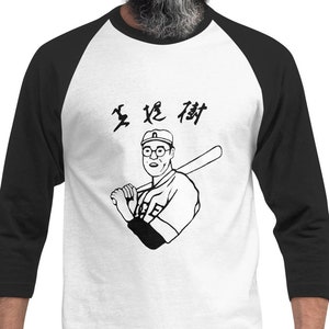Puede incluir: Una camiseta de béisbol blanca y negra con una ilustración de dibujos animados de un hombre con gafas y sosteniendo un bate de béisbol. El texto "生 投 13" está impreso en la camiseta.