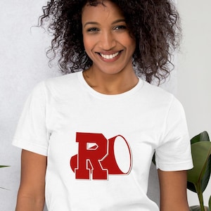 Può includere: Maglietta bianca con una lettera "R" rossa e una grafica di megafono rossa.