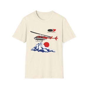 Könnte beinhalten: Cremefarbenes T-Shirt mit einer Grafik eines rot-schwarzen Hubschraubers, einer Bergkette und einer roten Sonne. Der Text "AIR SERVICES INTERNATIONAL" befindet sich über dem Hubschrauber.