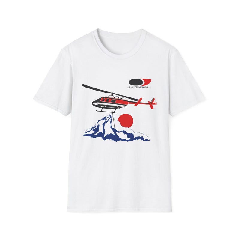 Peut inclure: T-shirt blanc avec un motif d'h&eacute;licopt&egrave;re rouge et noir, d'un soleil rouge et de montagnes bleues. Le texte "AIR SERVICES INTERNATIONAL" est au-dessus de l'h&eacute;licopt&egrave;re. Col rond.