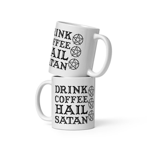 May include: Two white ceramic mugs stacked vertically. Each mug features black text that reads "DRINK COFFEE HAIL SATAN" in a bold, serif font. To the right of the text, there are three black pentagram symbols arranged in a vertical column.