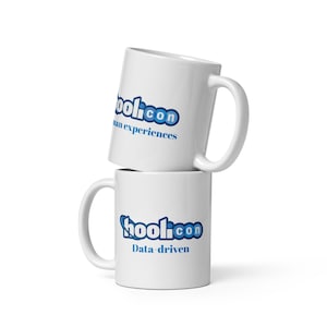 Peut inclure: Deux mugs en céramique blancs empilés. Le mug du dessus affiche le texte "hool.con" en bleu, avec "human experiences" en dessous. Le mug du dessous porte "hool.con" en bleu, avec "Data-driven" en dessous.
