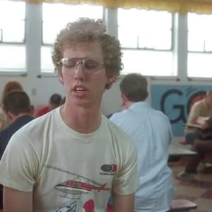 Peut inclure: Une personne porte un t-shirt blanc avec un motif d'h&eacute;licopt&egrave;re et des lunettes rectangulaires. La personne est dans une caf&eacute;t&eacute;ria scolaire avec d'autres &eacute;l&egrave;ves. Le t-shirt a un motif d'h&eacute;licopt&egrave;re rouge et blanc.