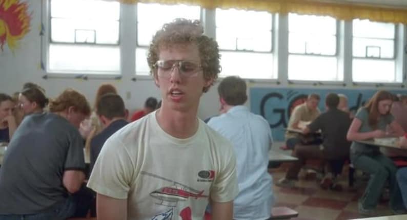 Peut inclure: Une personne porte un t-shirt blanc avec un motif d'h&eacute;licopt&egrave;re et des lunettes rectangulaires. La personne est dans une caf&eacute;t&eacute;ria scolaire avec d'autres &eacute;l&egrave;ves. Le t-shirt a un motif d'h&eacute;licopt&egrave;re rouge et blanc.