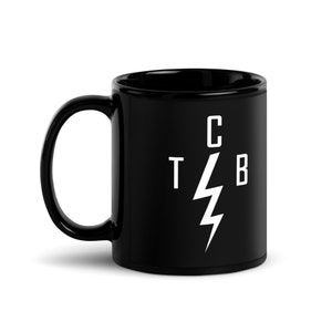 Puede incluir: Taza de café de cerámica negra con un gráfico de rayo blanco y las letras "CTB" alrededor.