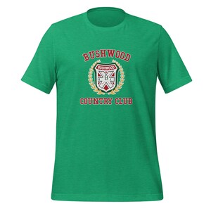 May include: Green t-shirt with a white and red logo that says "Bushwood Country Club". The logo features a shield with a crossed golf club and the text "Bushwood" inside.