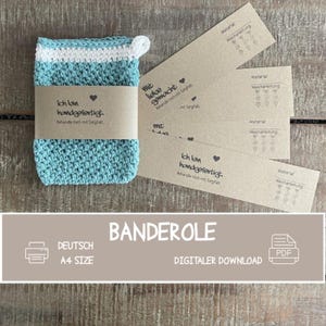 Puede incluir: Una bolsa rectangular tejida a ganchillo en color verde azulado y blanco con un pequeño lazo, envuelta en una banda de papel marrón con el texto en alemán 'Ich bin handgefertigt. Behandle mich con Sorgfalt.' Varias etiquetas de papel marrón a juego.
