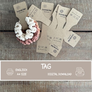 May include: A crochet scrunchie featuring a two-tone design of cream and dusty rose yarn, displayed on a brown cardboard tag labeled "scrunchie Handmade" with care instructions. Several additional blank cardboard tags are arranged nearby.