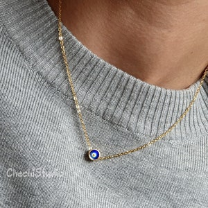 May include: A gold chain necklace with a small blue evil eye charm.