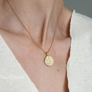 May include: A gold chain necklace with a round, textured pendant. The pendant has a detailed design.