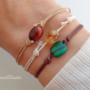 May include: Three bracelets with different colored beads. The bracelets are made of brown, beige, and white cord. The beads are red, orange, and green.